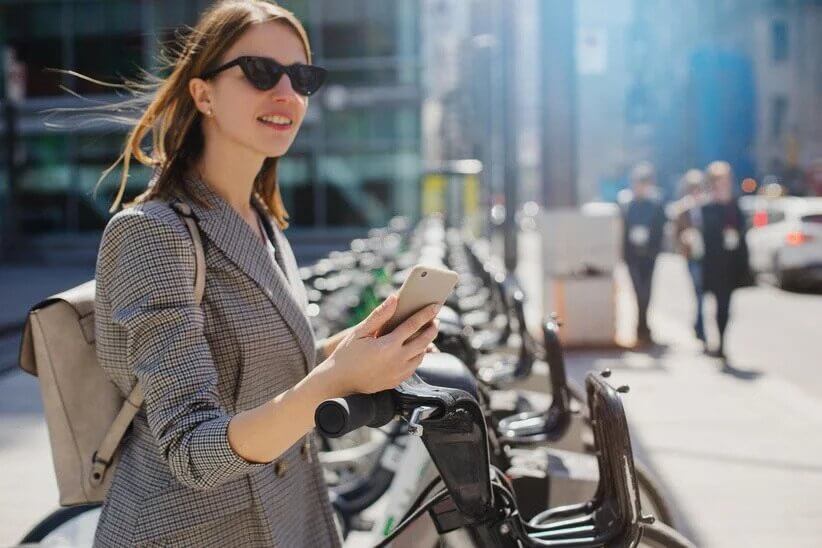 girl with a phone in front of a bikesharing station - top bike sharing Q&A 